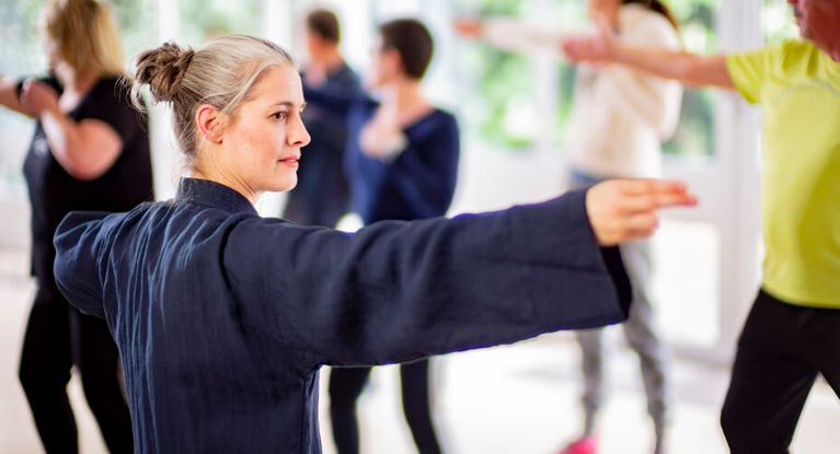 Therapeutin und Patientengruppe beim gemeinsamen Tai-Chi in der Sporthalle