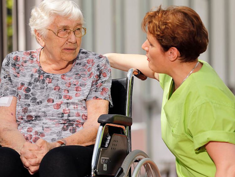 Patientin im Rollstuhl spricht mit Pflegekraft