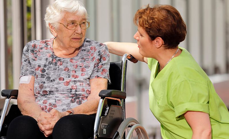 Patientin im Rollstuhl spricht mit Pflegekraft