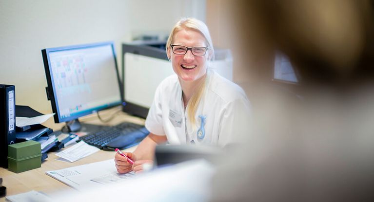 Lachende Pflegekraft sitzt an einem Schreibtisch