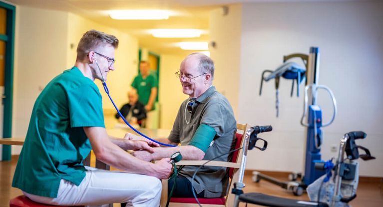 Junge männliche Pflegekraft misst bei einem geriatrischen Patienten den Blutdruck