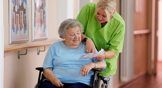 Geriatrische Patientin im Rollstuhl spricht mit Pflegekraft