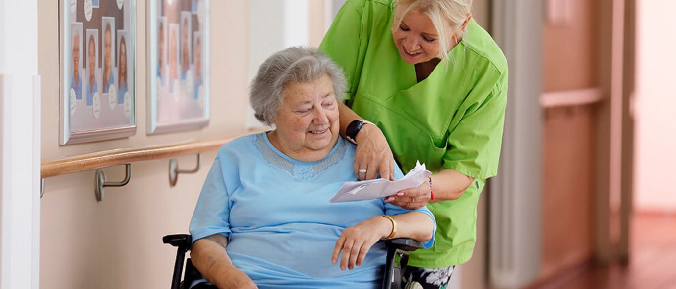 Geriatrische Patientin im Rollstuhl spricht mit Pflegekraft
