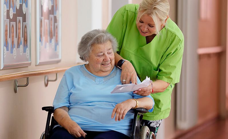 Geriatrische Patientin im Rollstuhl spricht mit Pflegekraft